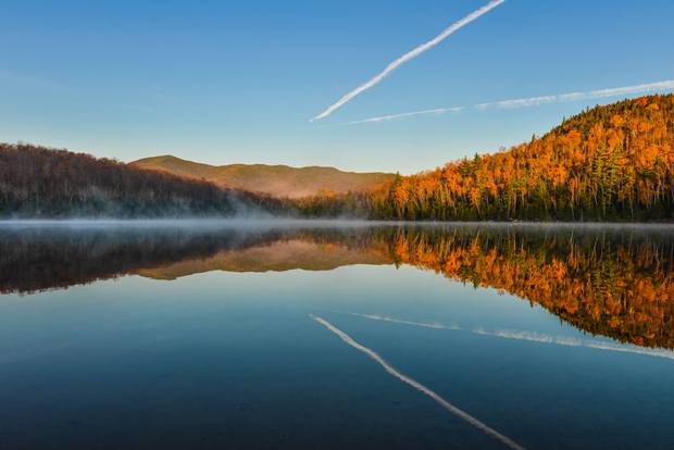 Lake Reflections of fall foliage. Colorful autumn leaves shed reflected on the calm waters of Heart Lake in Lake Placid